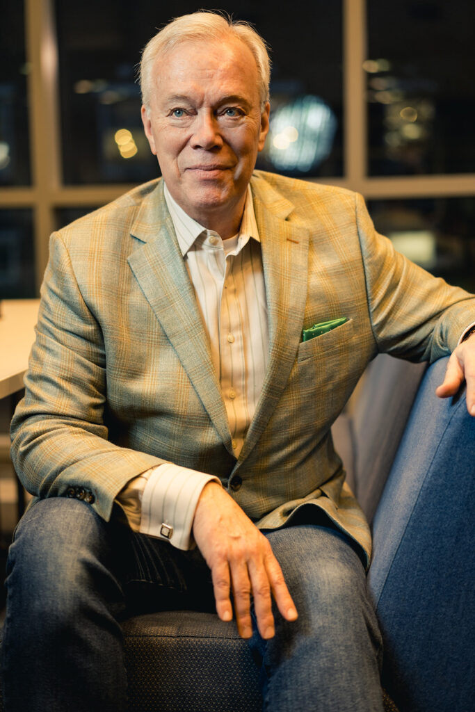 Portrait of a man in a suit, sitting on a chair.