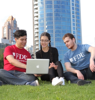 Three students sitting on the lawn looking at a laptop