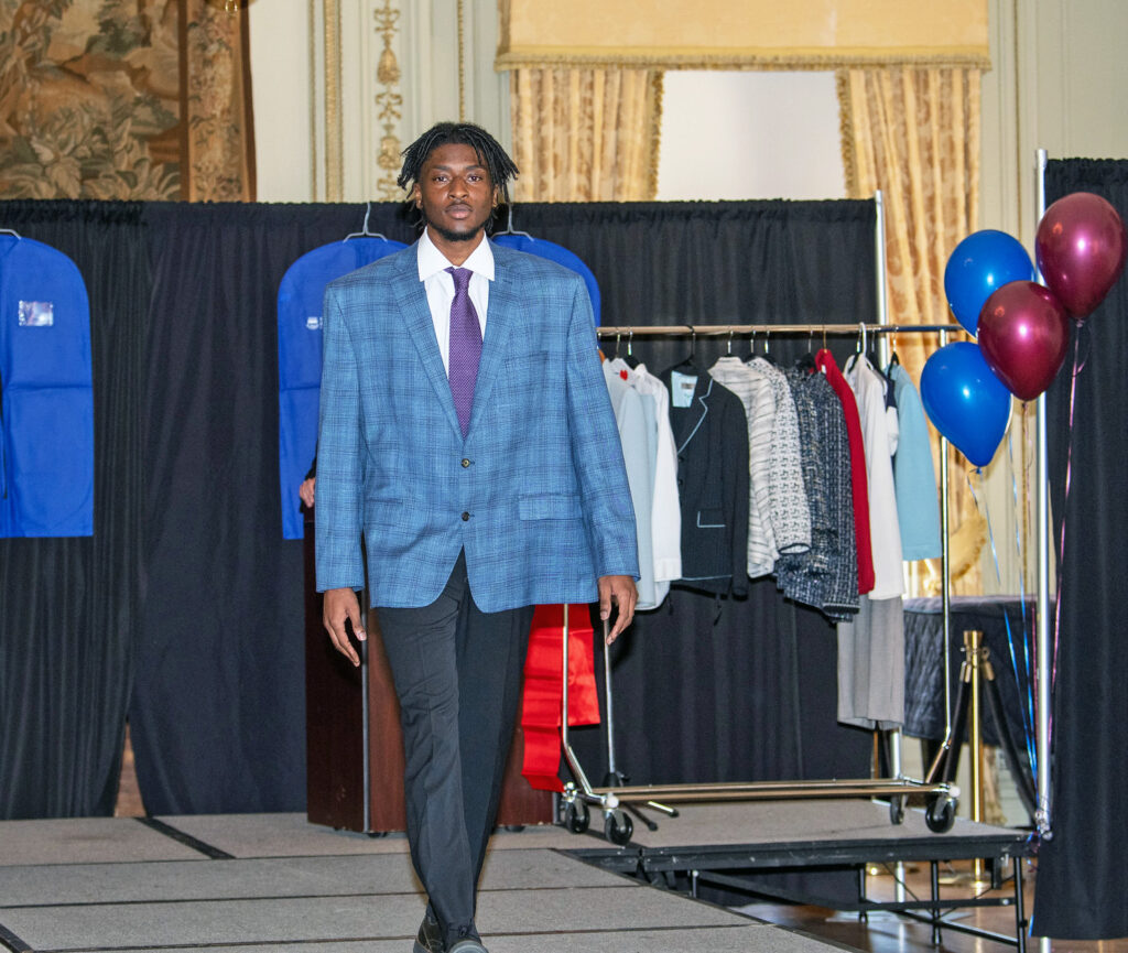 A male model walks down the runway to model men's businesswear.