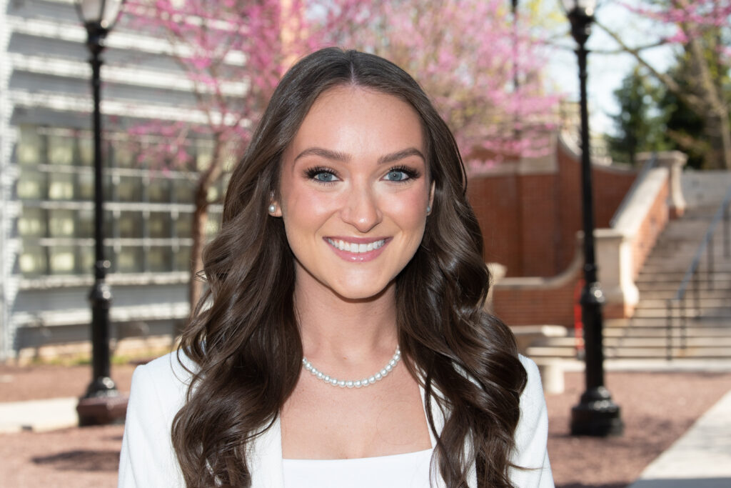 Taylor Bellardino, wearing a pearl necklace and pearl earrings, poses for a photo outside.