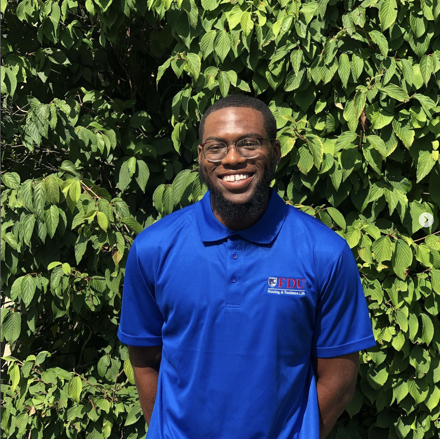 Portrait of a young man in a polo shirt, with greenery behind him.