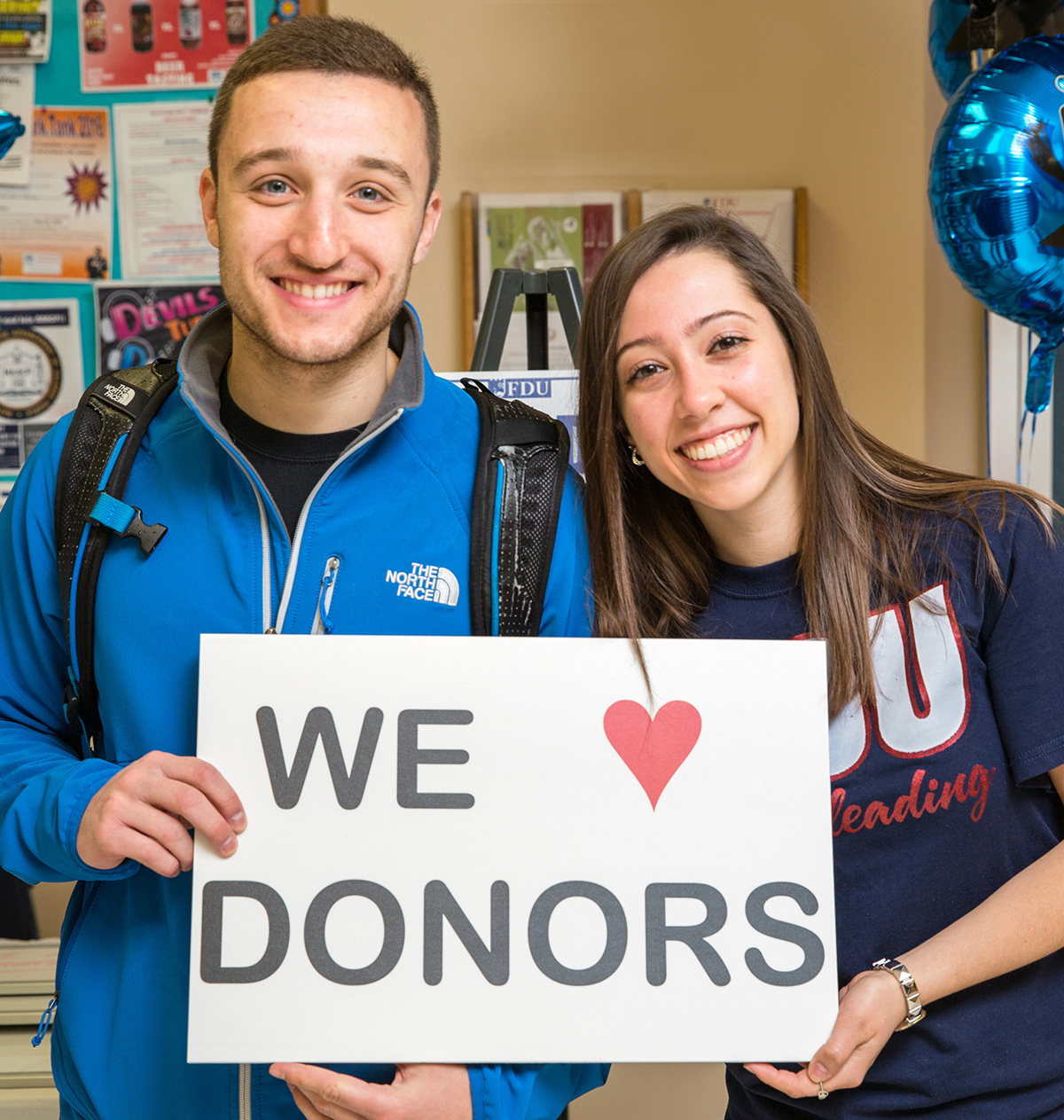 A male student and a female student hold up a sign that reads we love donors.