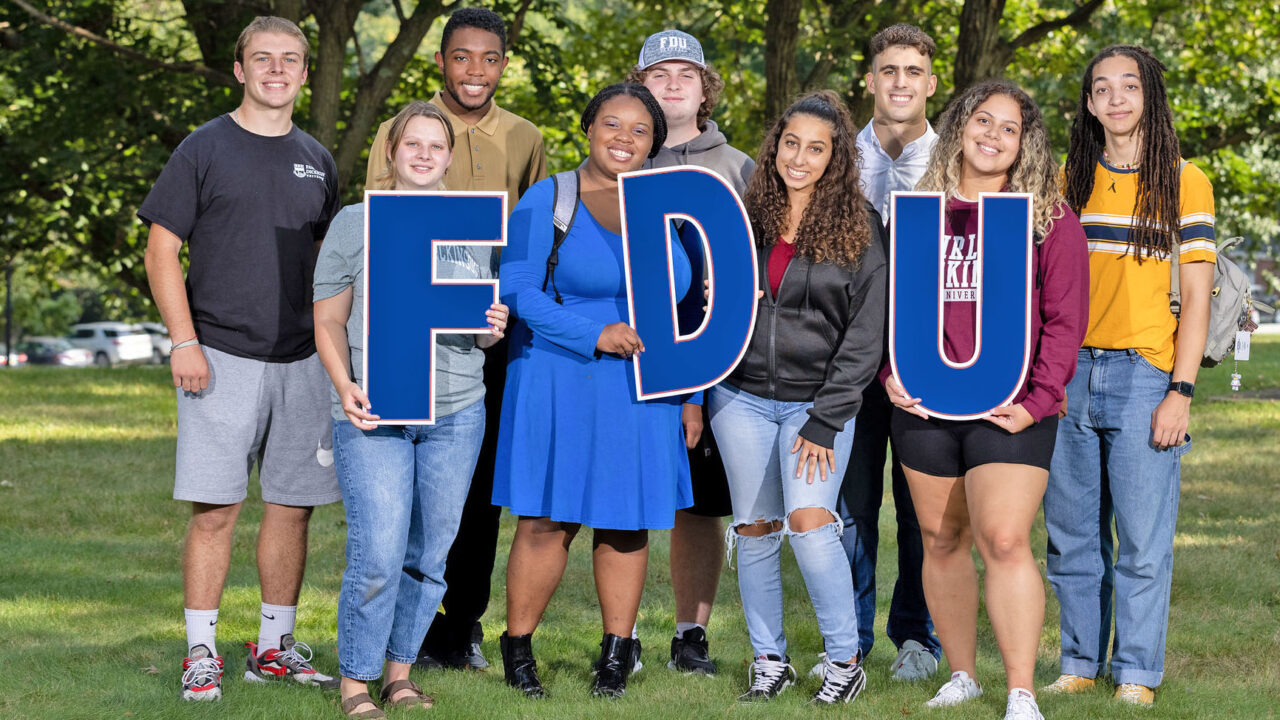 Smiling students hold up letters spelling F-D-U.