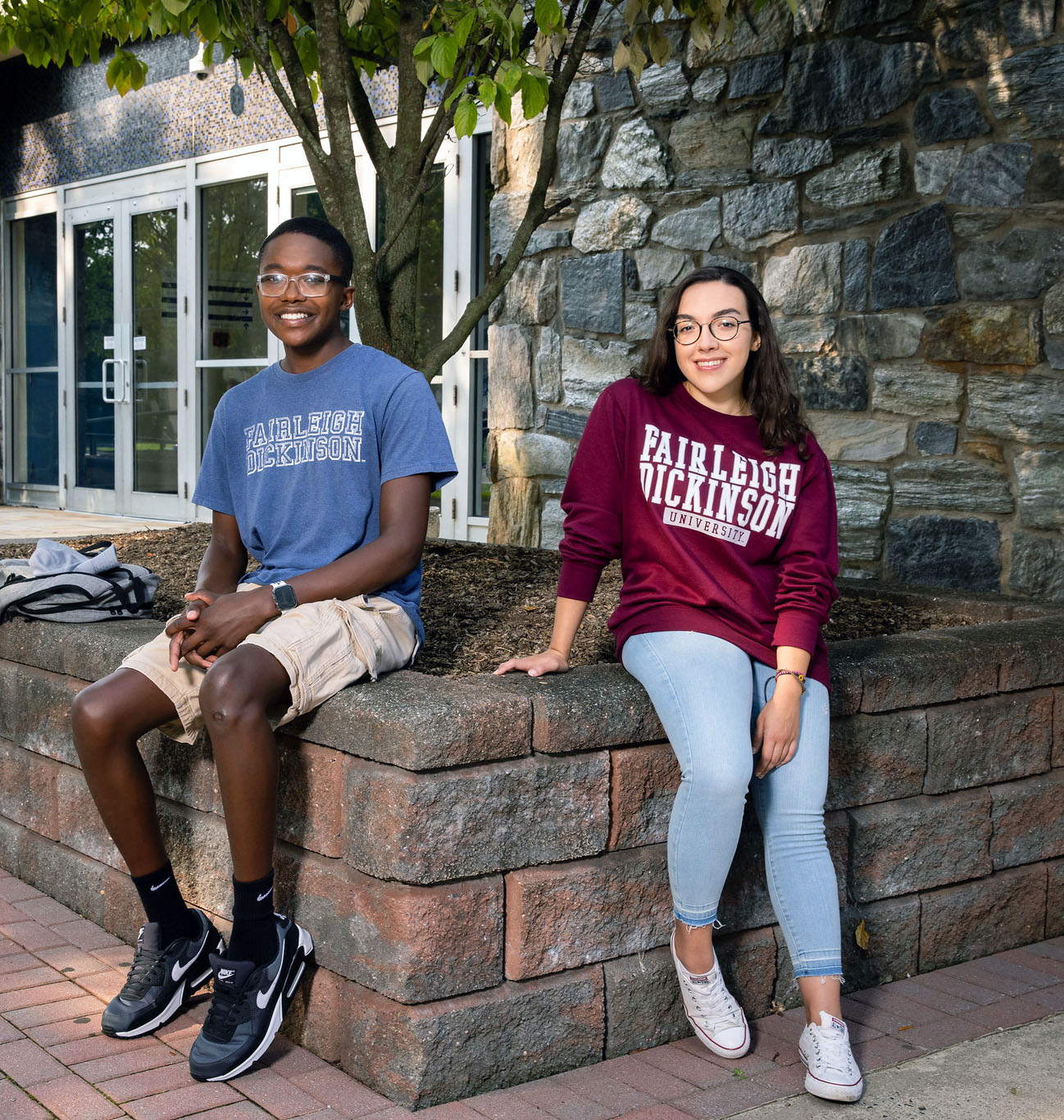 Two students sit outside a stone building.