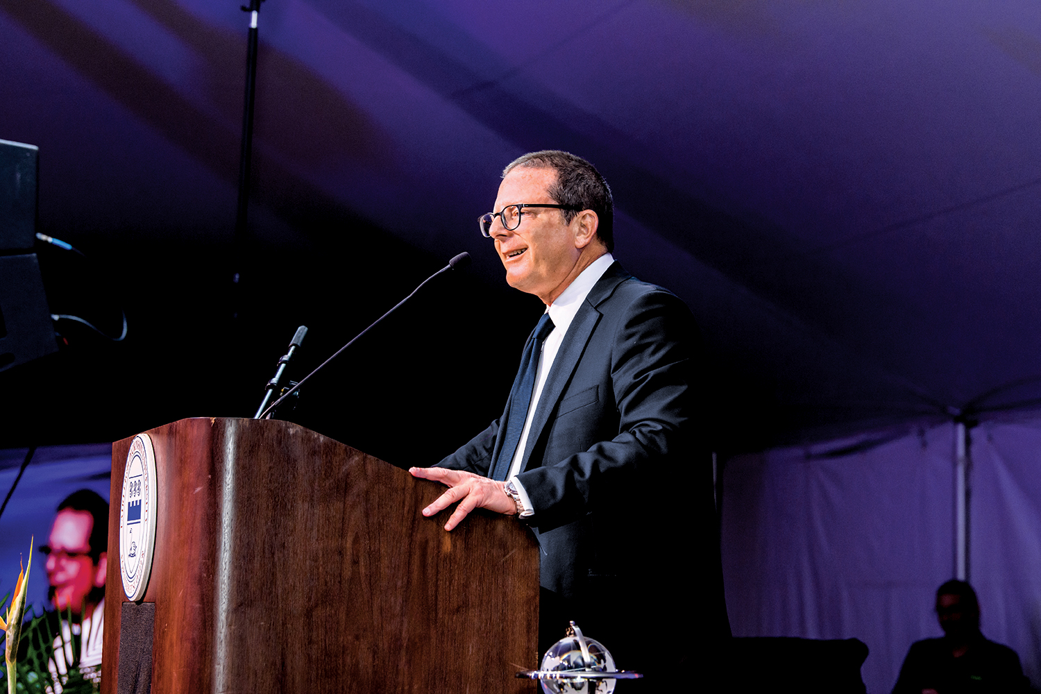 A man wearing glasses and a suit and tie delivers remarks at a podium.