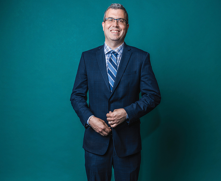 Portrait of a man in a suit and tie against a teal green backdrop.