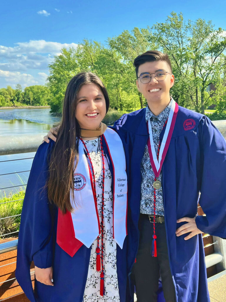 Two graduates, one female and one male, dressed in graduation robes and cords.