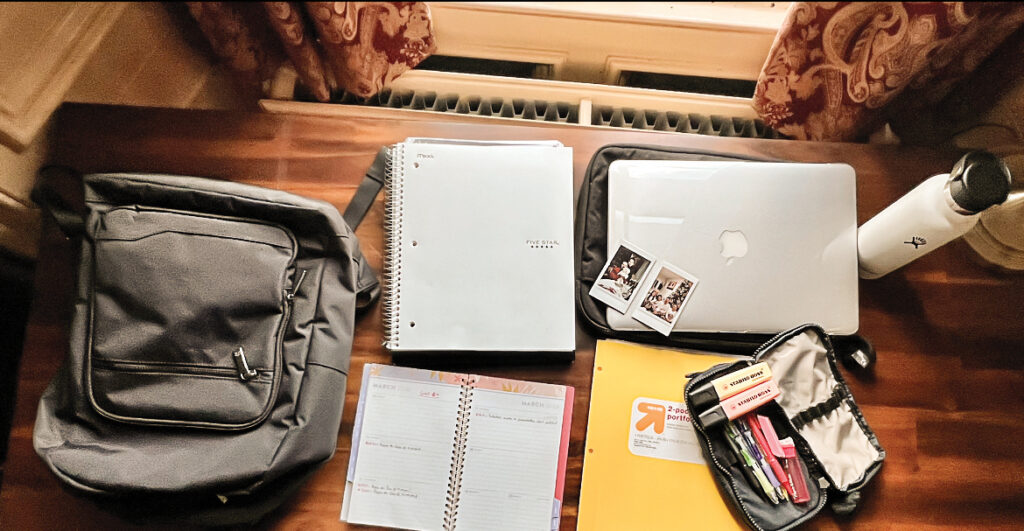 Study supplies, a laptop, and Polaroid snapshots sit on a desk.