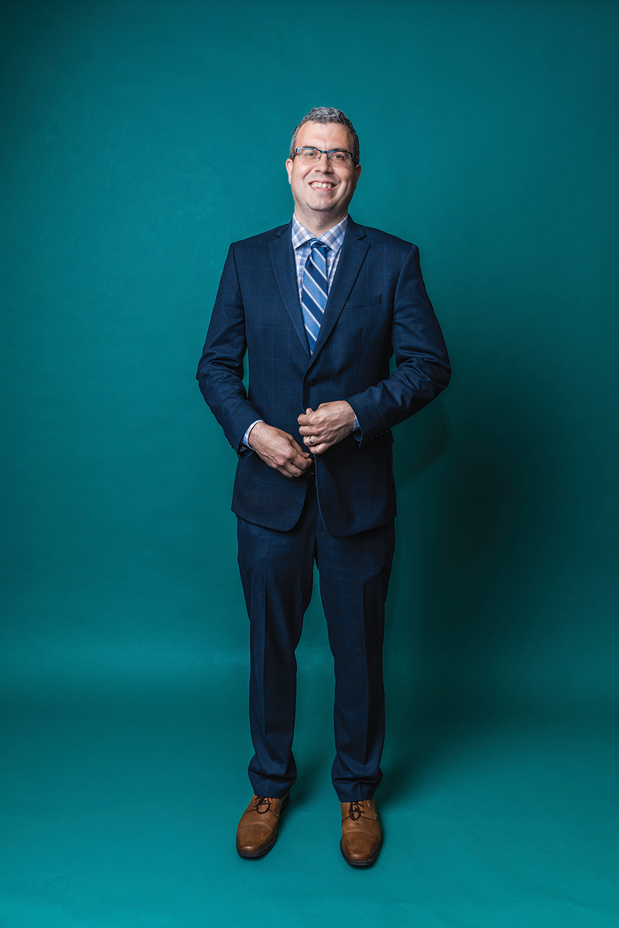 Portrait of a man in a suit and tie against a teal green backdrop.