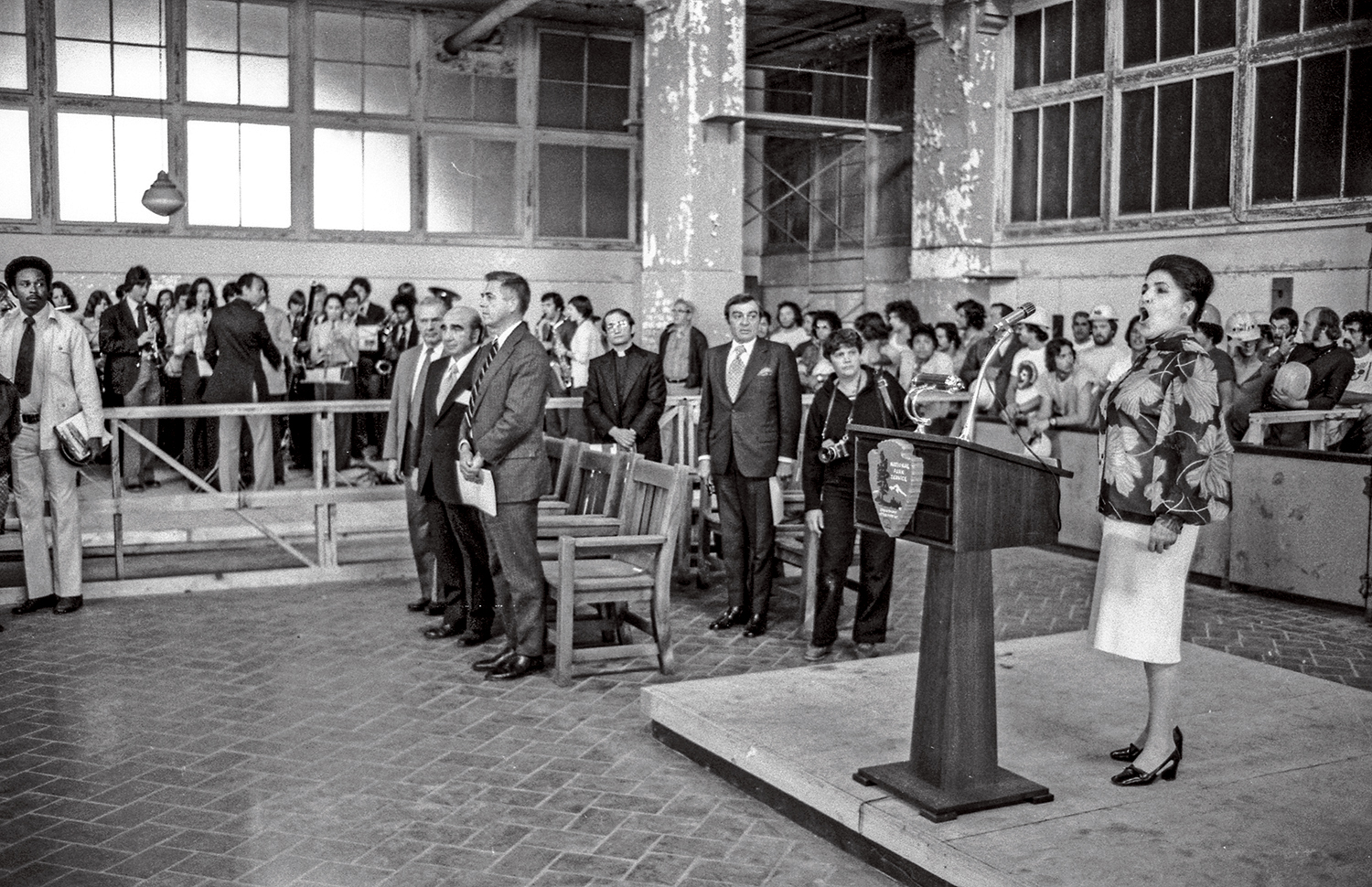A woman stands singing at a podium in Ellis Island.