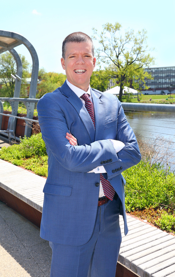 A man wearing a suit stands with his arms crossed on the Metropolitan Campus footbridge.