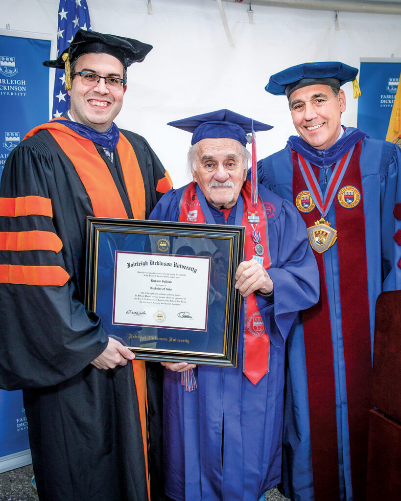 Three men stand in graduation robes and hold up a diploma.