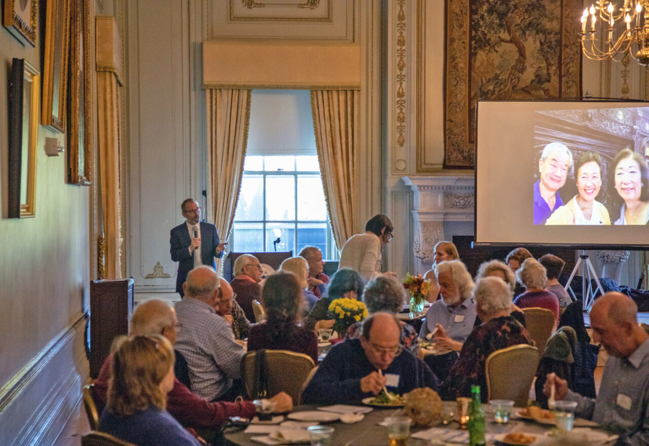 A man at a podium addresses a crowd of guests.