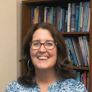 Portrait of a woman standing in front of a bookcase.