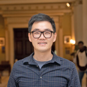 Portrait of a man, standing inside and wearing glasses.