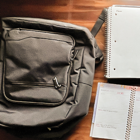 A backpack and notebook lie open on a table.