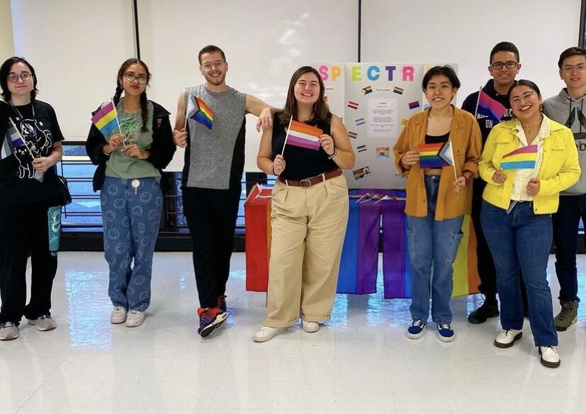 students hold various LGBTQIA+ and smile at the camera