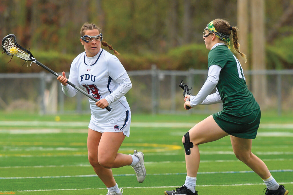 Two female lacrosse players with lacrosse sticks face off before preparing to pass the ball. 