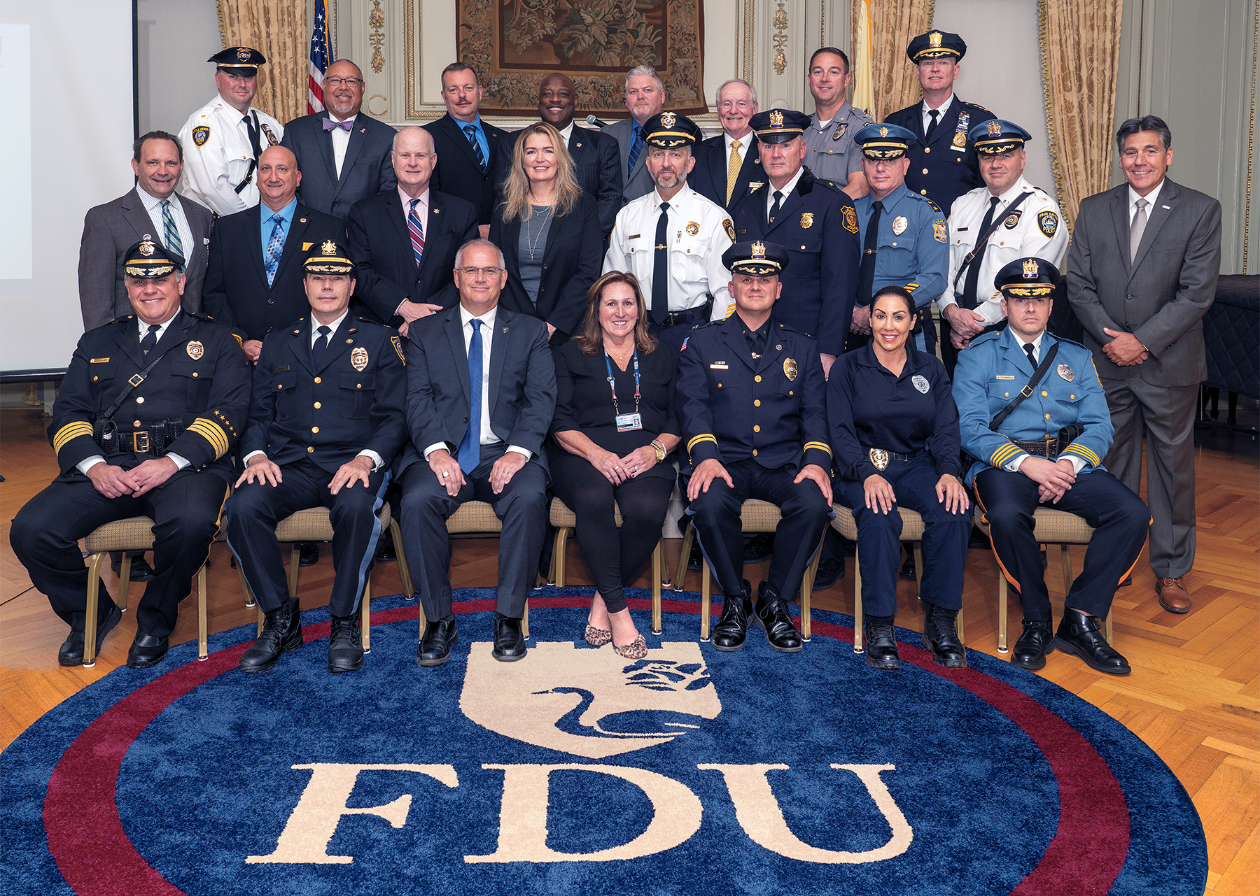 A group of men and woman wearing suits and police uniforms, pose for a group photo.