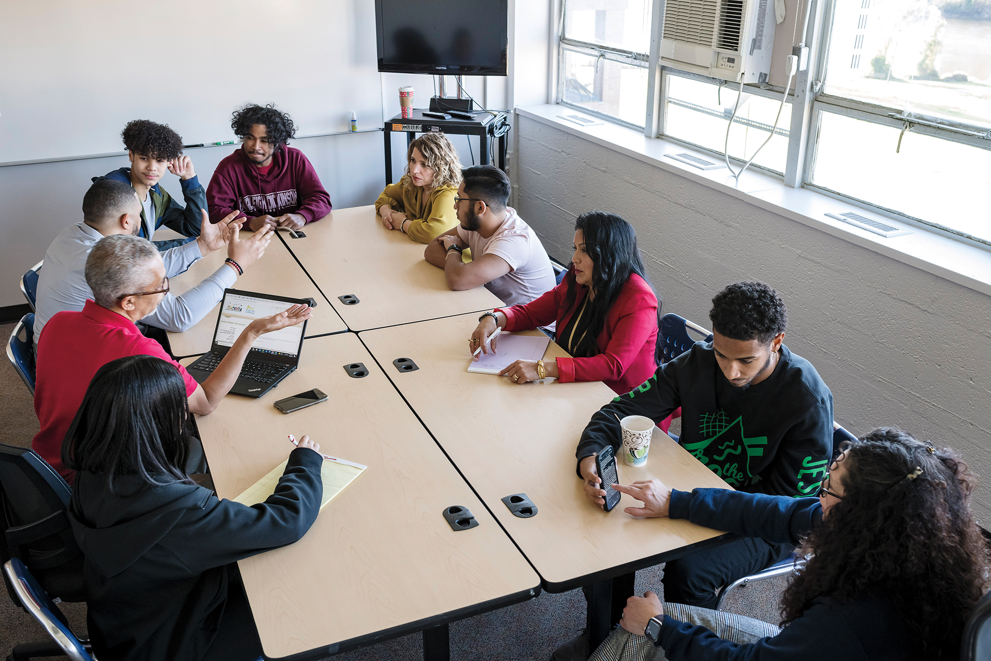 A group of faculty, students and staff sit and meet at a conference table.