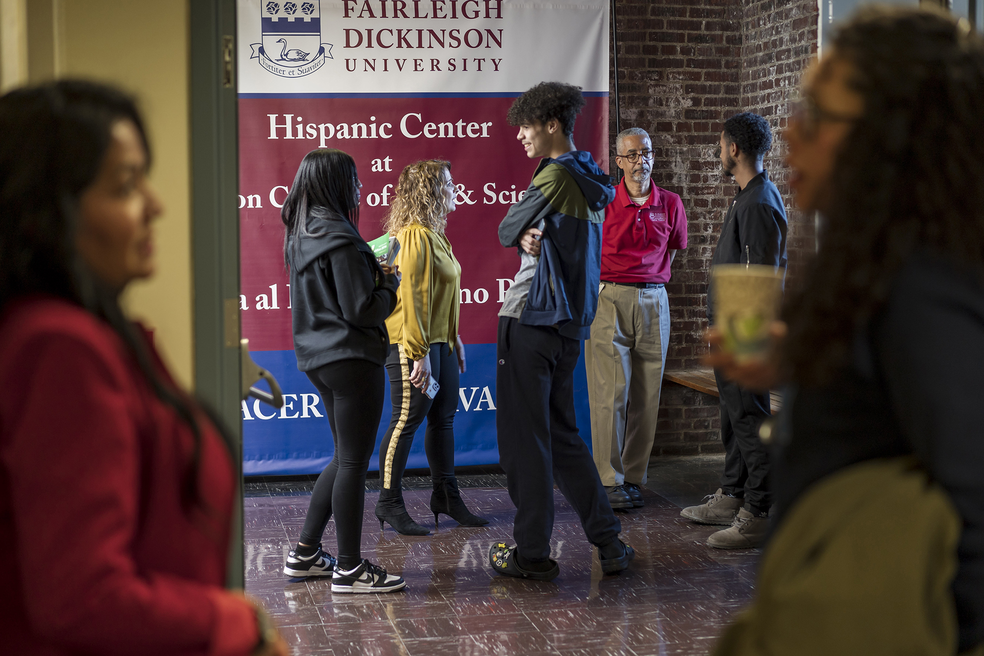 A group of students, faculty and administrators mill in a hallway. A banner sign behind them reads, "Hispanic Center."