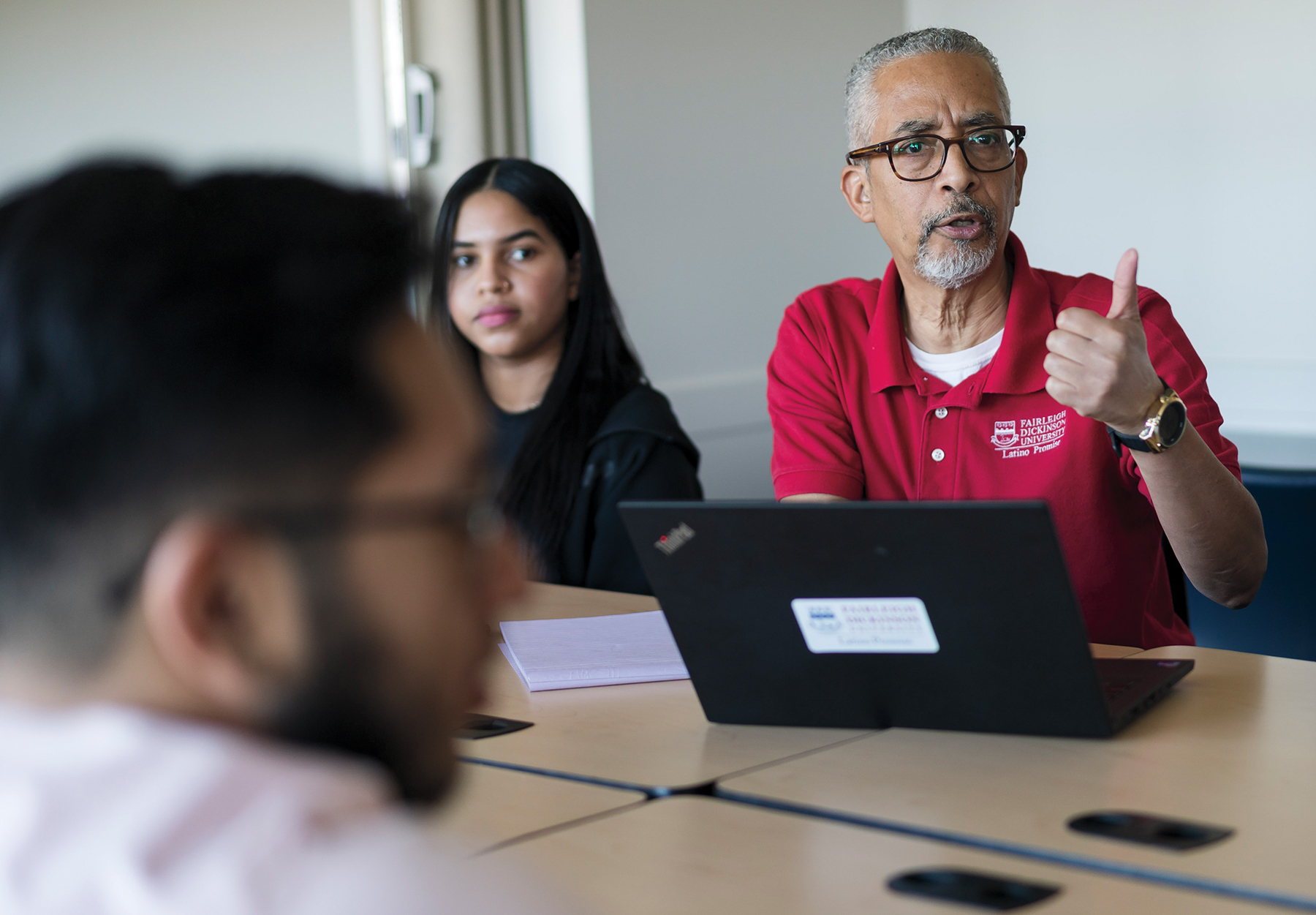 A man with a laptop in front of him gestures as he talks.