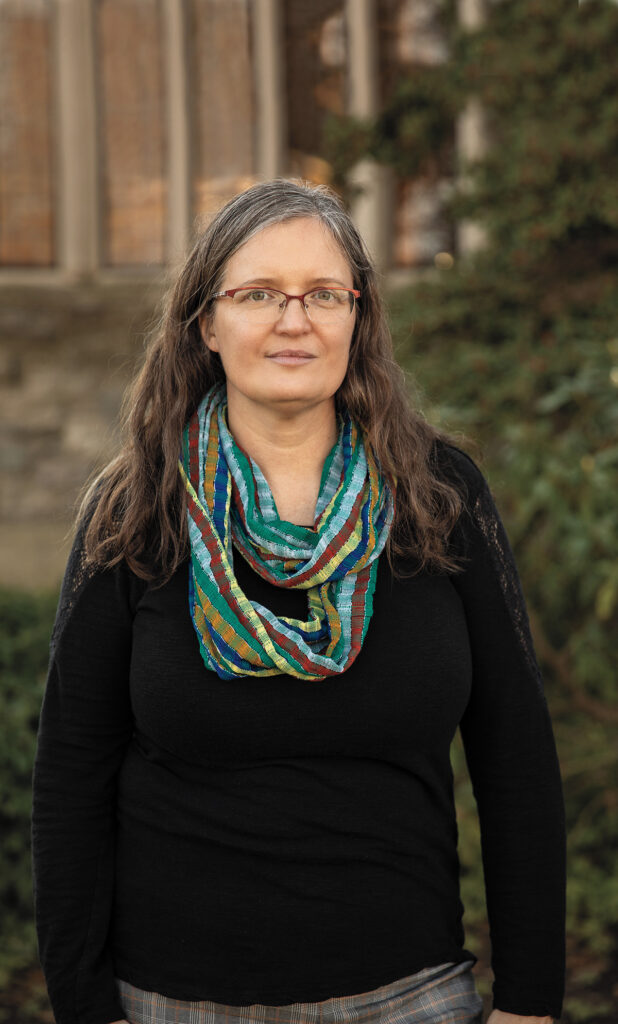 Portrait of a woman wearing a colorful scarf and glasses. She is standing outside.