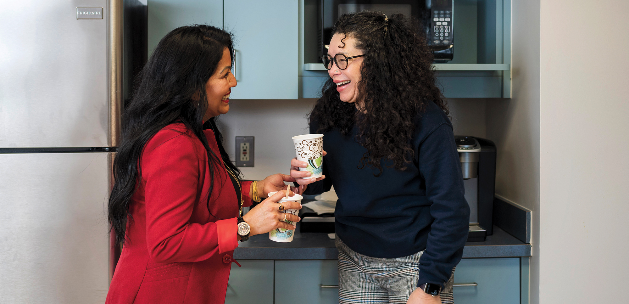 Two women holding coffees, share a chat and a laugh.