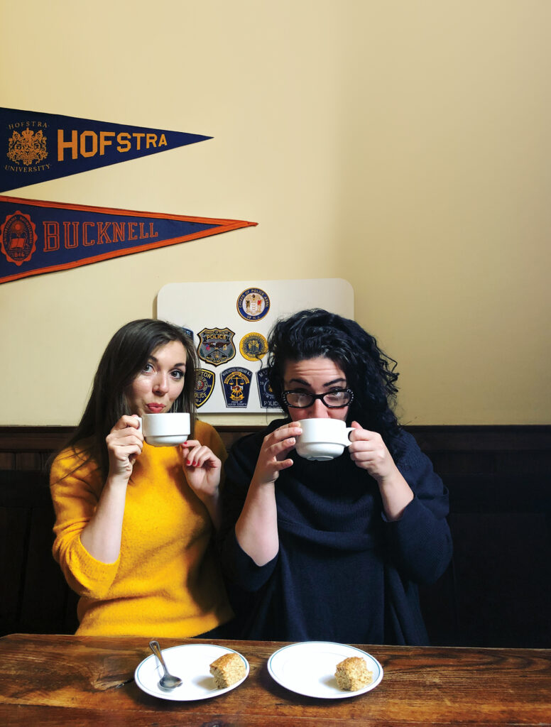 Two young women sip tea.