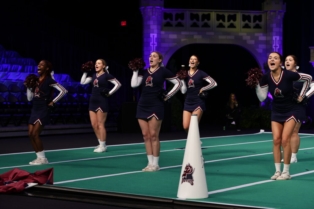 The cheerleading team yells out their cheer while holding pom poms. 