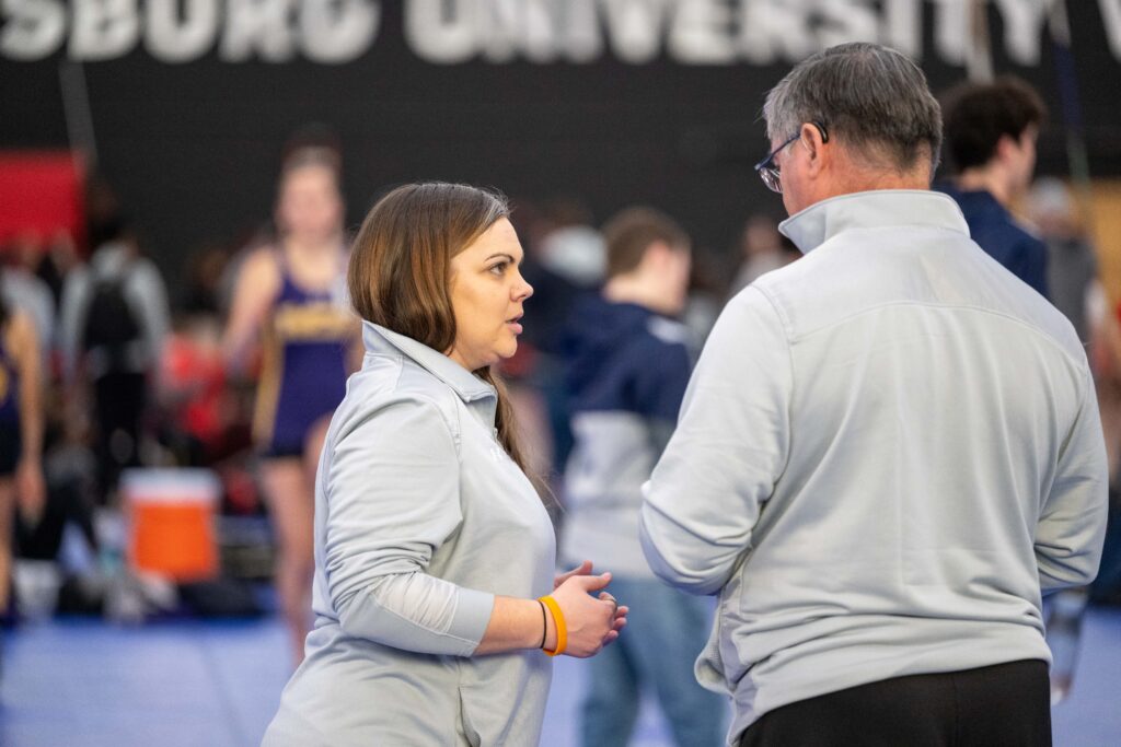 A woman and a man in light grey sweatshirts stand together talking. 