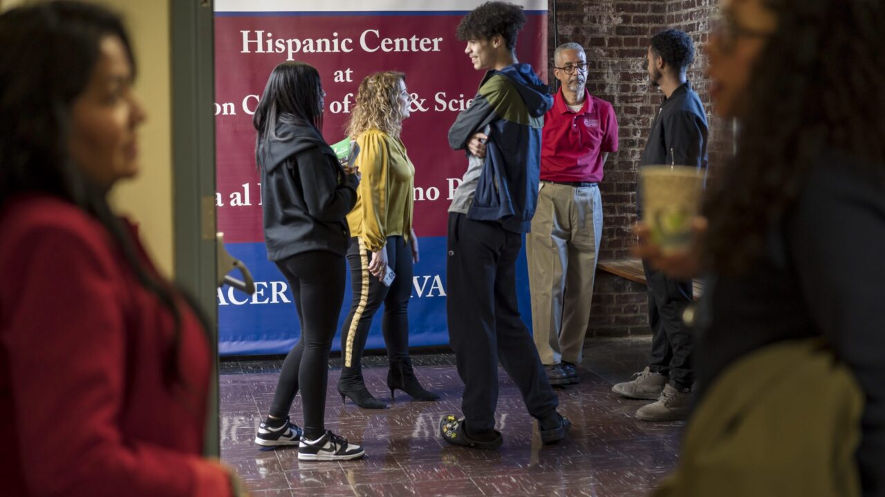 The image shows people in front of the Hispanic Center sign, conveying information about the center and its activities.
