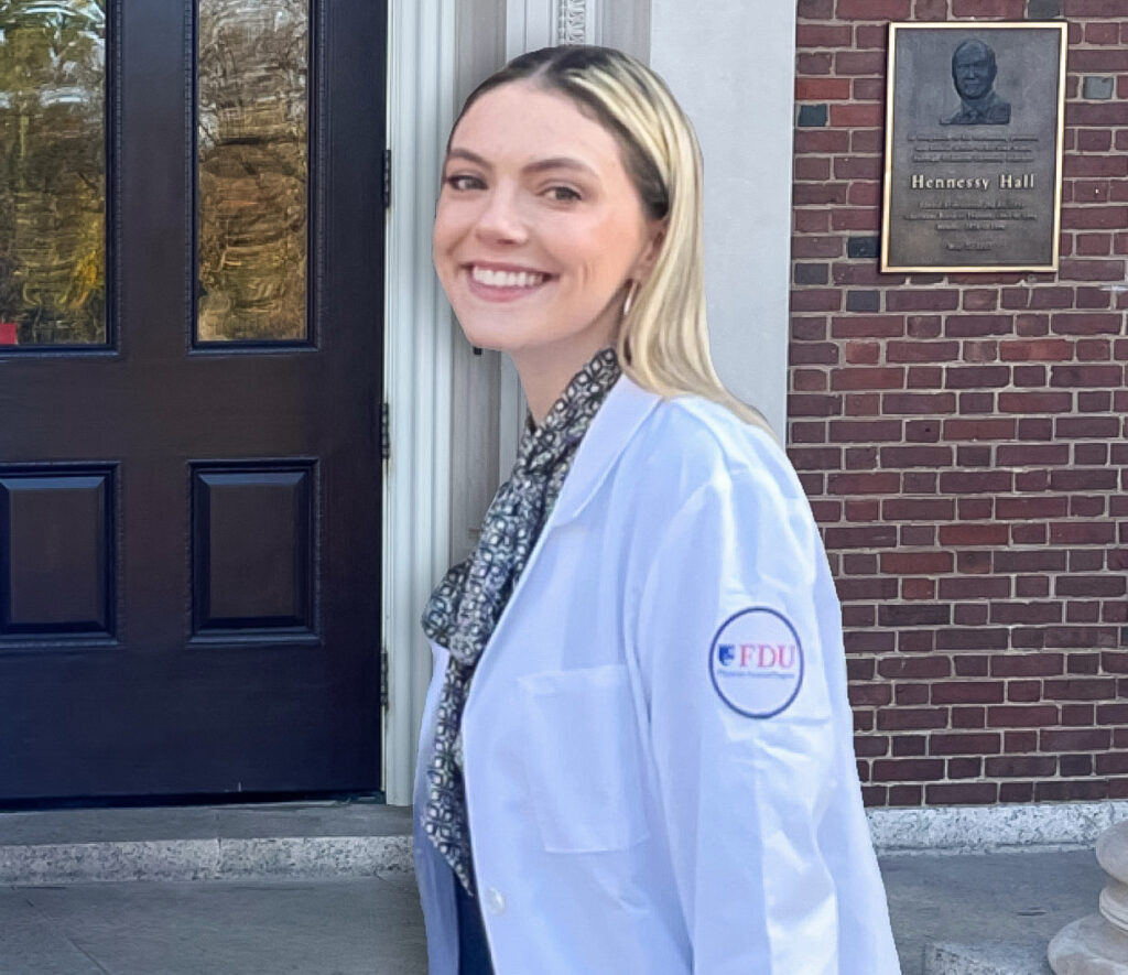 A young woman wearing a white coat stands in front of Hennessy Hall.