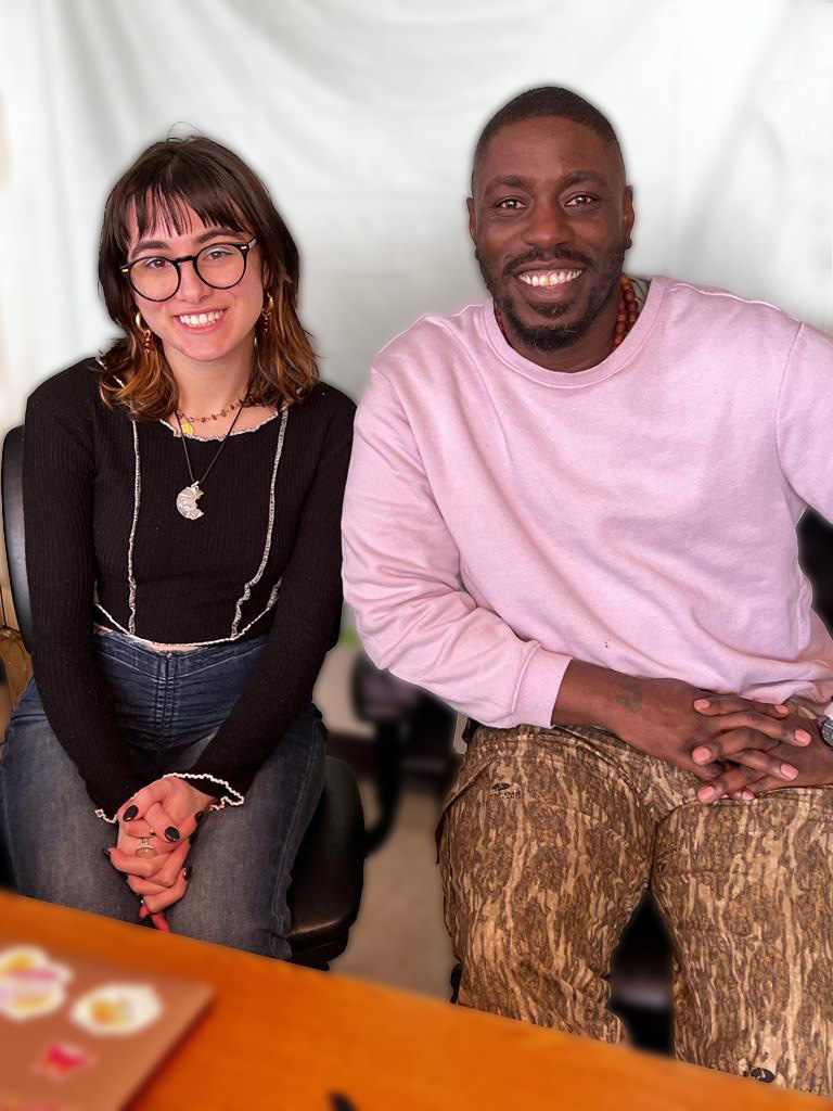 A woman and a man sit in desk chairs and pose for a photo. Both smile broadly.