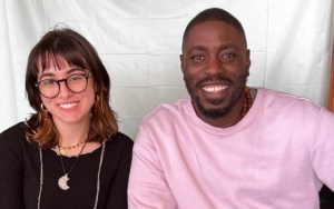 A woman and a man sit in desk chairs and pose for a photo. Both smile broadly.