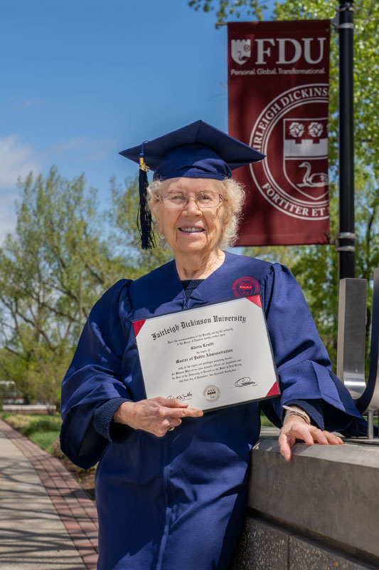 A 90-year-old graduate in Commencement regalia holds up her diploma.