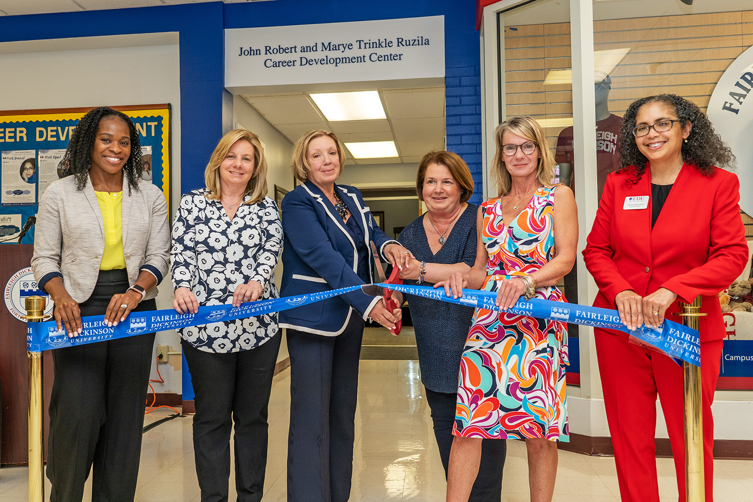 Six women stand in a line, ready to cut a ribbon with large ceremonial scissors.