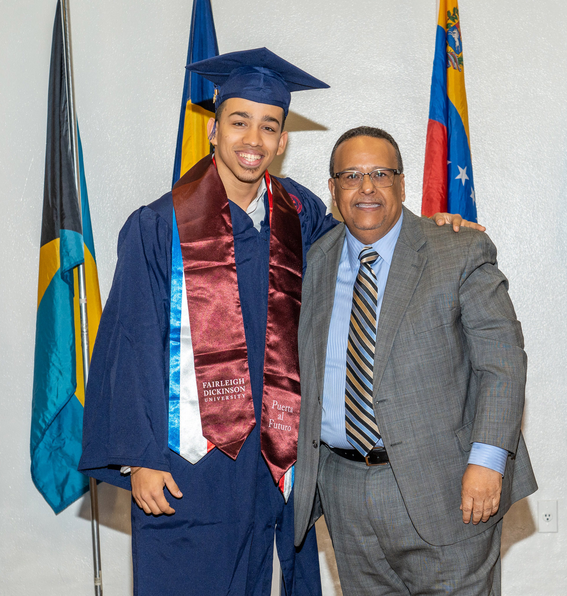 Two men, one in a cap and gown, and one in a suit, pose for a photo.