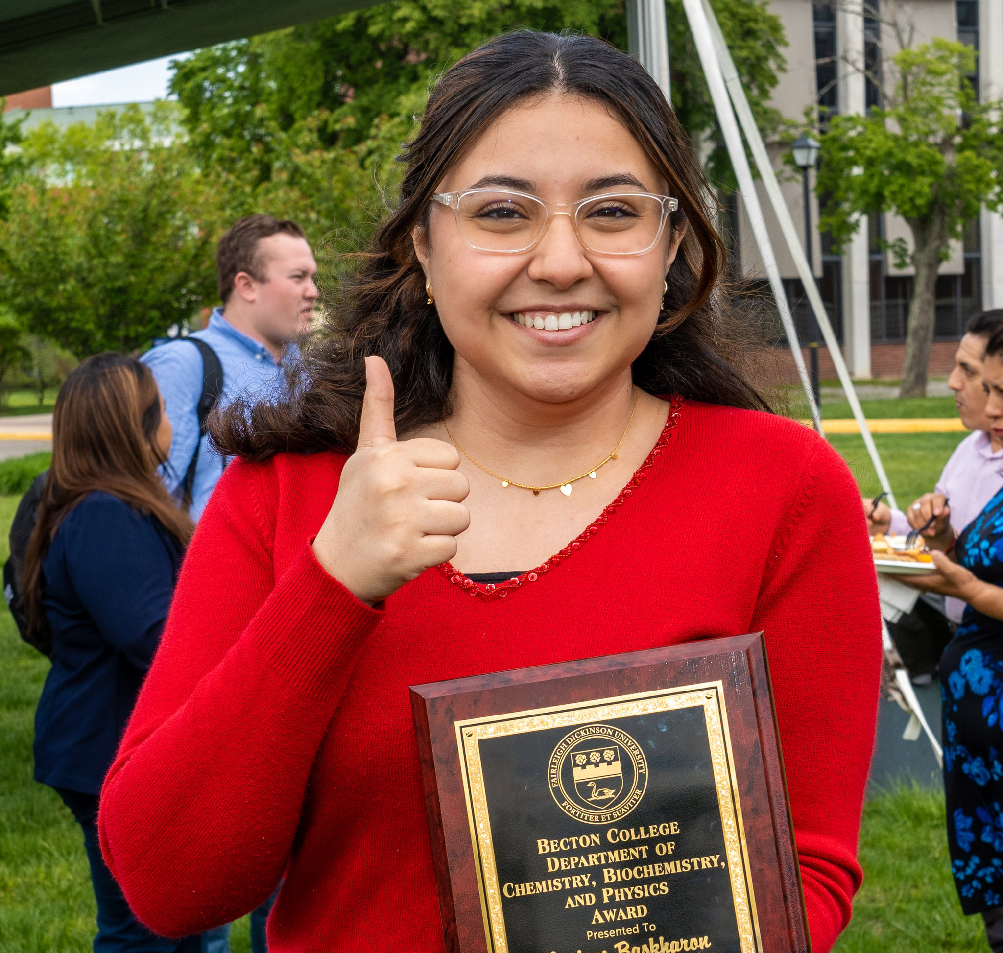 A young woman holding up an award gives a thumbs up.