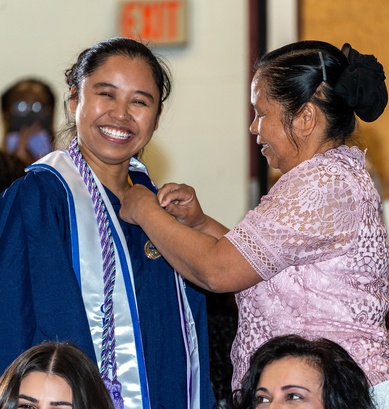 A woman pins a pin on a smiling nursing graduate.