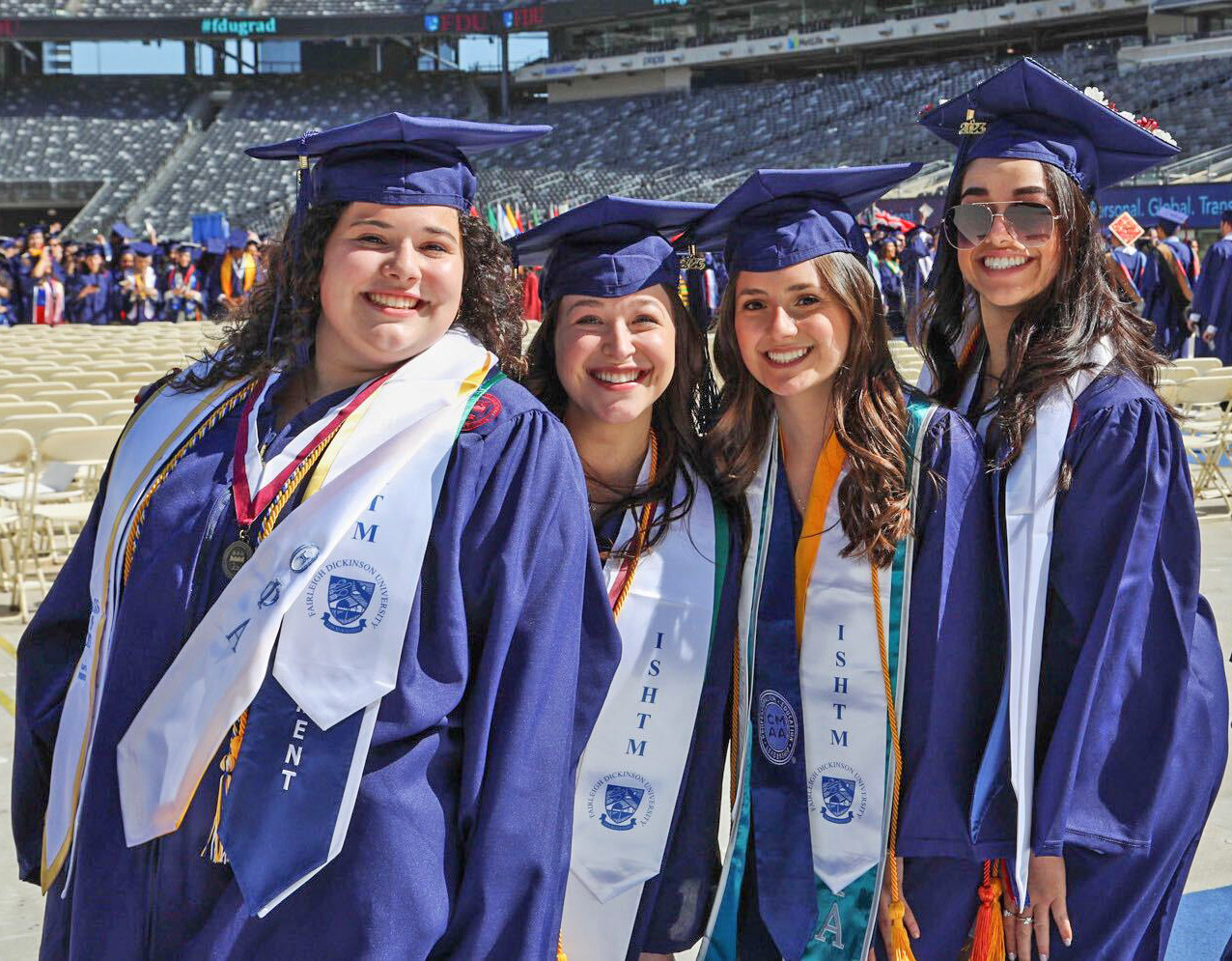 Four female graduates, wearing caps, gowns and sashes, pose for a photo.