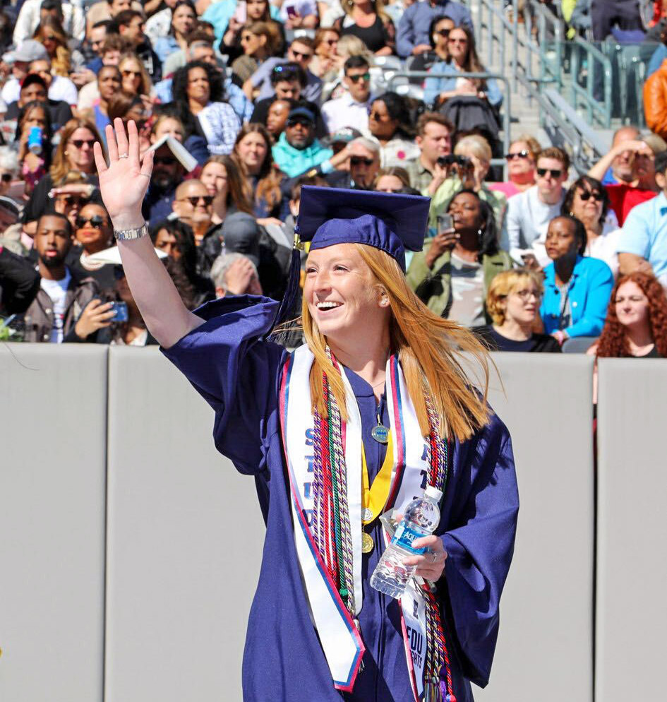 A female graduate waves to the crowd on graduation day.