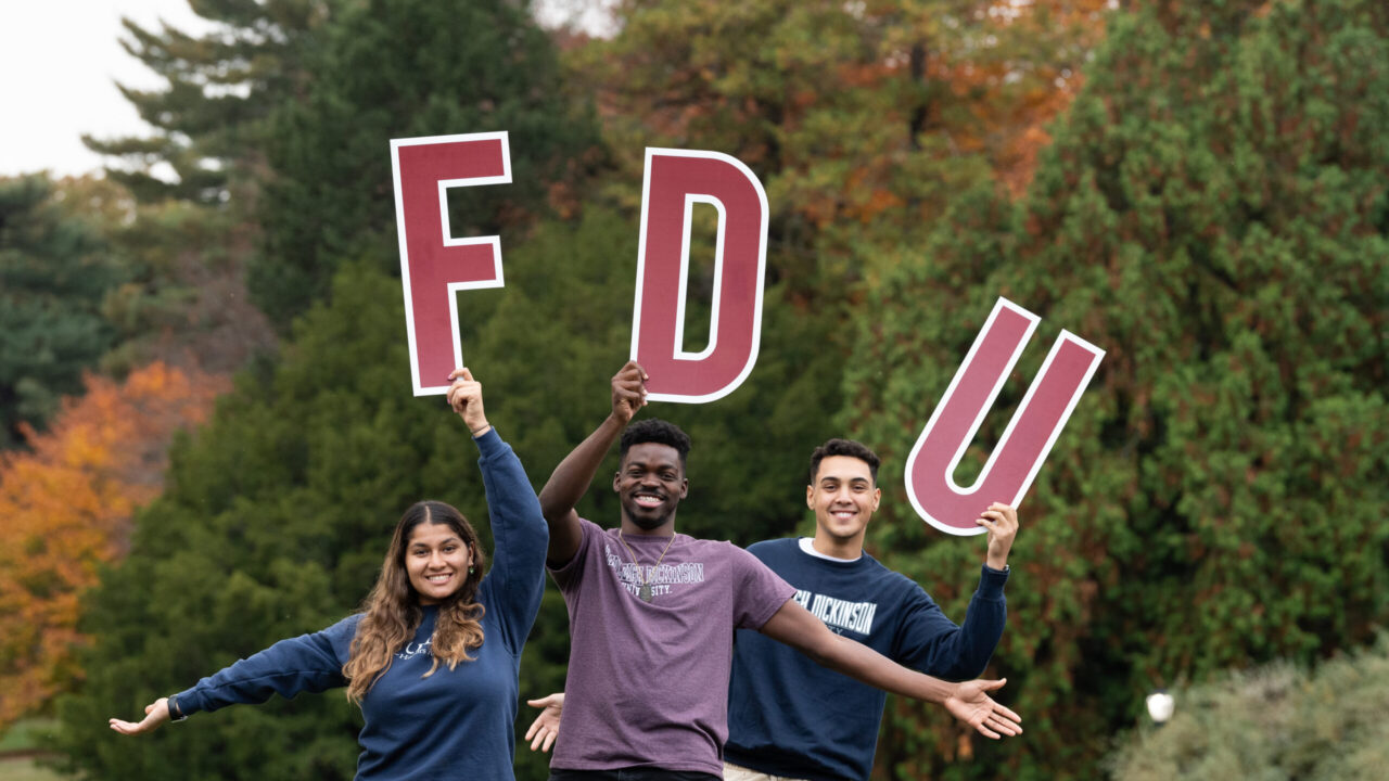 Three students stand with FDU letters on the Florham Campus.