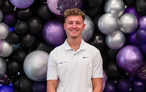 Portrait photo of a young man in casual clothes, posing in front of a balloon wall.