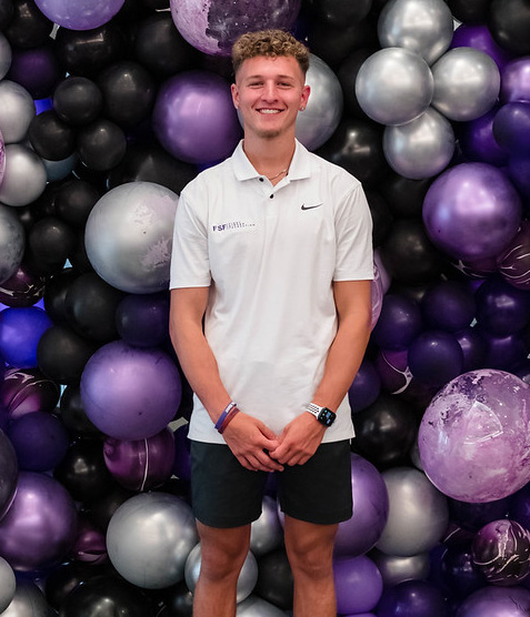 Portrait photo of a young man in casual clothes, posing in front of a balloon wall.