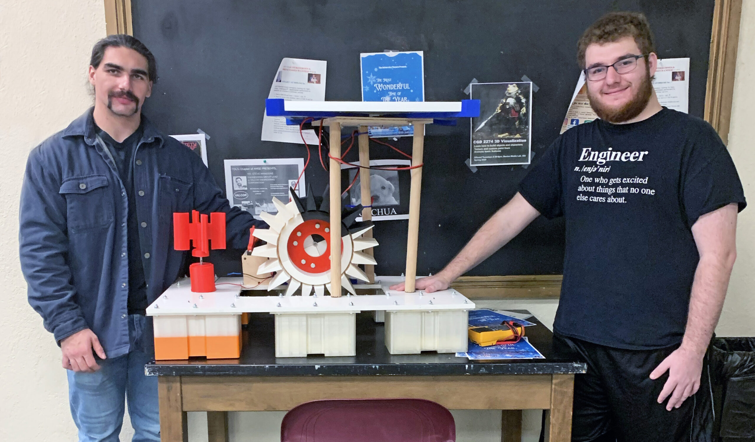 Two young male engineers flank the green energy device they designed and constructed. It collects solar, wind and hydro power.