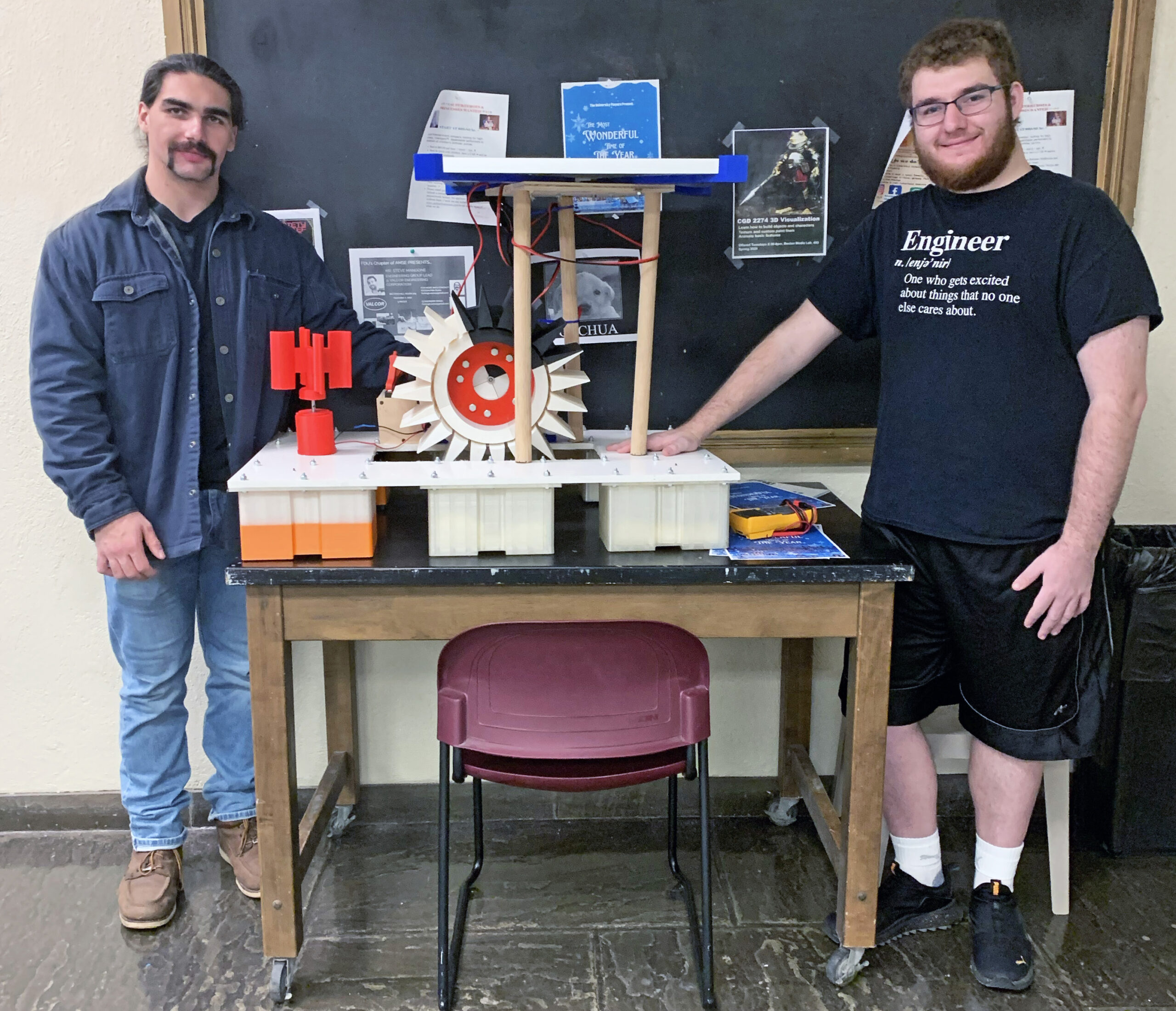 Two young male engineers flank the green energy device they designed and constructed. It collects solar, wind and hydro power.