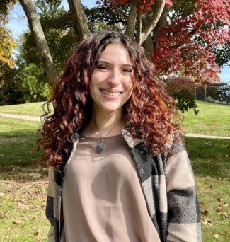 student stands in front of autumn trees