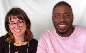 A woman and a man sit in desk chairs and pose for a photo. Both smile broadly.