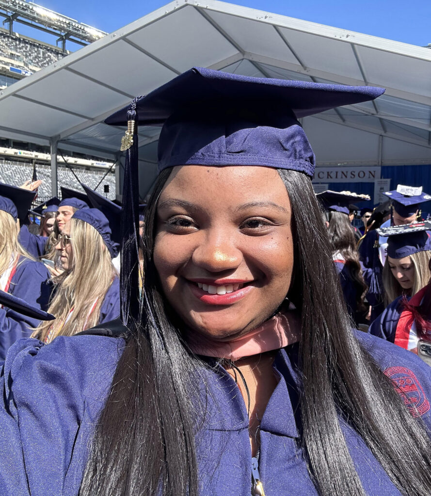 A female graduate wearing a cap and gown, takes a selfie at graduation.